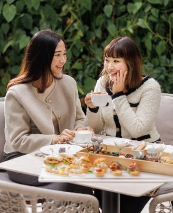 Two women sitting at a table with food and drinksAI-generated content may be incorrect.