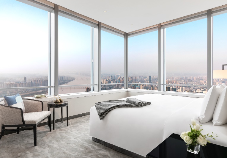 A bedroom with large windows and a city view

Description automatically generated